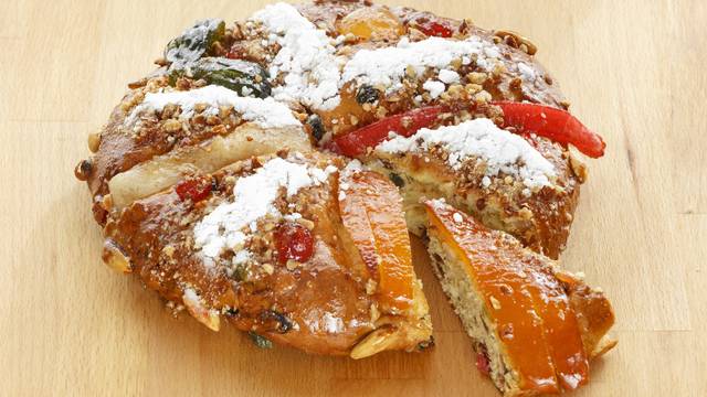 Traditioneller portugiesischer Weihnachtskuchen „Bolo Rei“ mit kandierten Früchten und Puderzucker auf einem Holzbrett